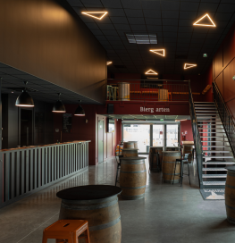 Espace intérieur de bar avec mezzanine, escalier métallique, tables tonneaux et plafond acoustique foncé