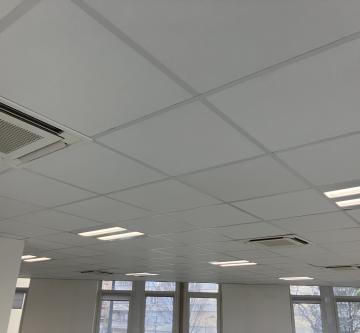 Plafond modulaire blanc avec dalles acoustiques et luminaires intégrés dans un espace de bureaux lumineux.