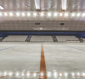 Patinoire intérieure équipée de dalles acoustiques au plafond, avec piste glacée vide et gradins en arrière-plan.