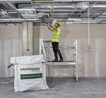 Plafond acoustique Eurocoustic installé dans un atelier de réemploi, avec un opérateur intervenant sur l’ossature technique en hauteur