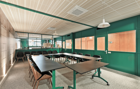 Salle de réunion moderne avec plafond acoustique à lames, murs verts et tables disposées en U.