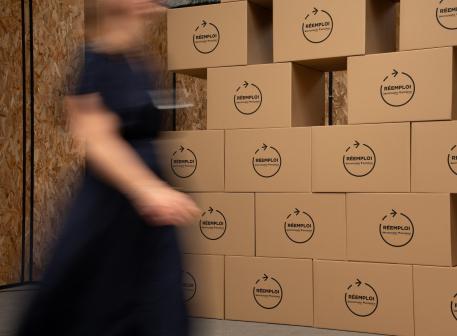 Personne passant devant un mur de cartons avec des dalles de réemploi Eurocoustic