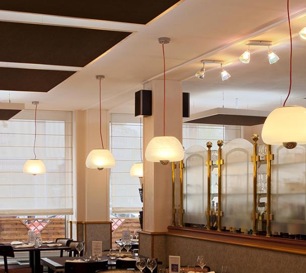 Interior of a modern restaurant featuring acoustic ceiling tiles for improved sound comfort, with warm lighting and contemporary decor.