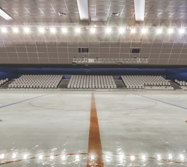 Patinoire intérieure équipée de dalles acoustiques au plafond, avec piste glacée vide et gradins en arrière-plan.