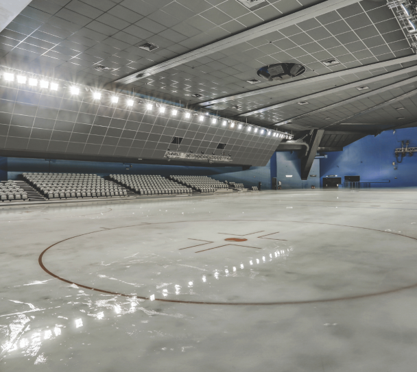 Patinoire intérieure équipée de dalles acoustiques au plafond, avec piste glacée vide et gradins en arrière-plan.