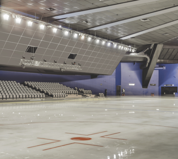 Patinoire intérieure équipée de dalles acoustiques au plafond, avec piste glacée vide et gradins en arrière-plan.