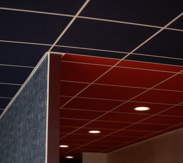 Gros plan sur un plafond modulaire acoustique Eurocoustic composé de dalles colorées bleues et rouges en trame apparente, intégrées dans un espace intérieur moderne avec éclairage encastré.