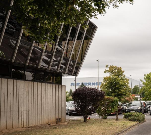 Vue extérieure du restaurant d’entreprise Air France avec façade vitrée contemporaine et environnement arboré. Le bâtiment accueille des espaces intérieurs équipés de plafonds modulaires acoustiques Eurocoustic.