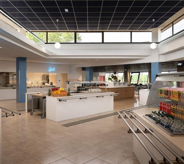 Vue d’ensemble du restaurant d’entreprise Air France avec espaces de restauration lumineux et îlots de service. Un plafond modulaire acoustique Eurocoustic sombre couvre la partie centrale de la pièce, contribuant au confort acoustique et à l’esthétique contemporaine de l’espace.