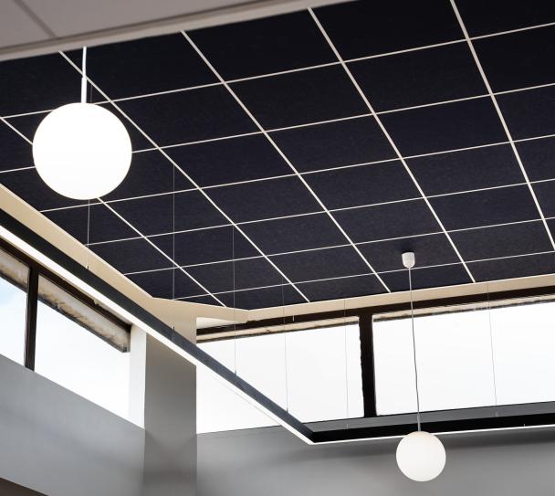 Détail architectural d’un plafond modulaire acoustique Eurocoustic bleu foncé installé sous une verrière, associé à des luminaires suspendus dans un espace de restauration lumineux.