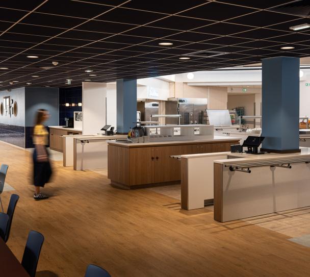Espace de restauration Air France avec mobilier contemporain et zones de service. Un plafond modulaire acoustique Eurocoustic noir à trame apparente habille l’ensemble du plafond et améliore le confort sonore des occupants.